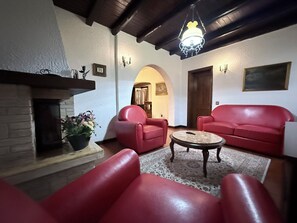 Un soggiorno con camino, divani in pelle rossa, un tavolino da caffè e un lampadario.