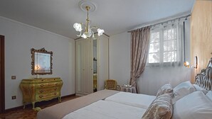 Ein Schlafzimmer mit einem großen Bett, einem Schminktisch, einem Stuhl und einem Fenster mit Vorhängen.