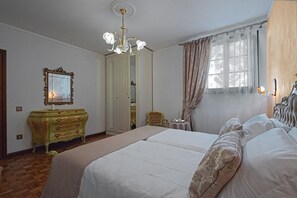 Une chambre à coucher avec un grand lit, une commode, une chaise et une fenêtre avec des rideaux.