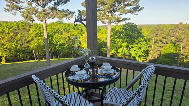 Une terrasse dotée d’une table et de deux chaises, entourée d’une rambarde, et offrant une vue sur une zone boisée.