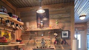 Une cuisine avec des murs en bois, un évier, une machine à café et diverses tasses et bouteilles disposées sur des étagères.