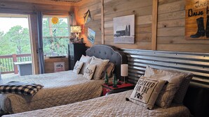 Une chambre de motel avec deux lits, un ventilateur de plafond, des murs en bois et une vue sur les arbres par la fenêtre.