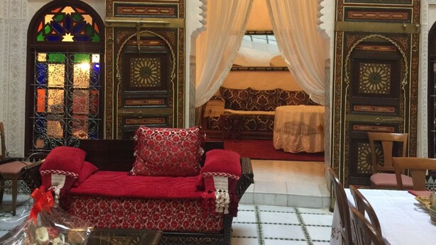 Una habitación marroquí tradicional con decoración elaborada, un sofá, una mesa de comedor y una cama con dosel.
