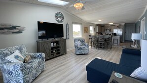 A spacious living room with a large flat-screen TV, a ceiling fan, and a dining area with a kitchen in the background. - Oceanfront 2Br 2Ba Condo with elevator and amazing views! (Surfside Beach)