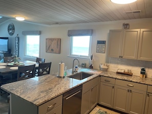 A kitchen with granite countertops, a sink, and cabinets. There are two windows with views of the ocean.