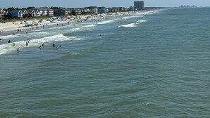 A beach with a row of buildings along the shore, a clear sky, and calm sea. - Oceanfront 2Br 2Ba Condo with elevator and amazing views! (Surfside Beach)