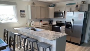 A modern kitchen with a central island, stainless steel appliances, and wooden bar stools. - Oceanfront 2Br 2Ba Condo with elevator and amazing views! (Surfside Beach)