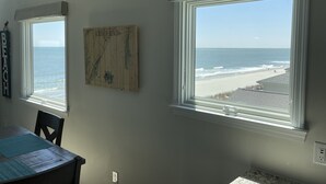 A room with two large windows overlooking a beach, a wooden table, and a wall-mounted map. - Oceanfront 2Br 2Ba Condo with elevator and amazing views! (Surfside Beach)