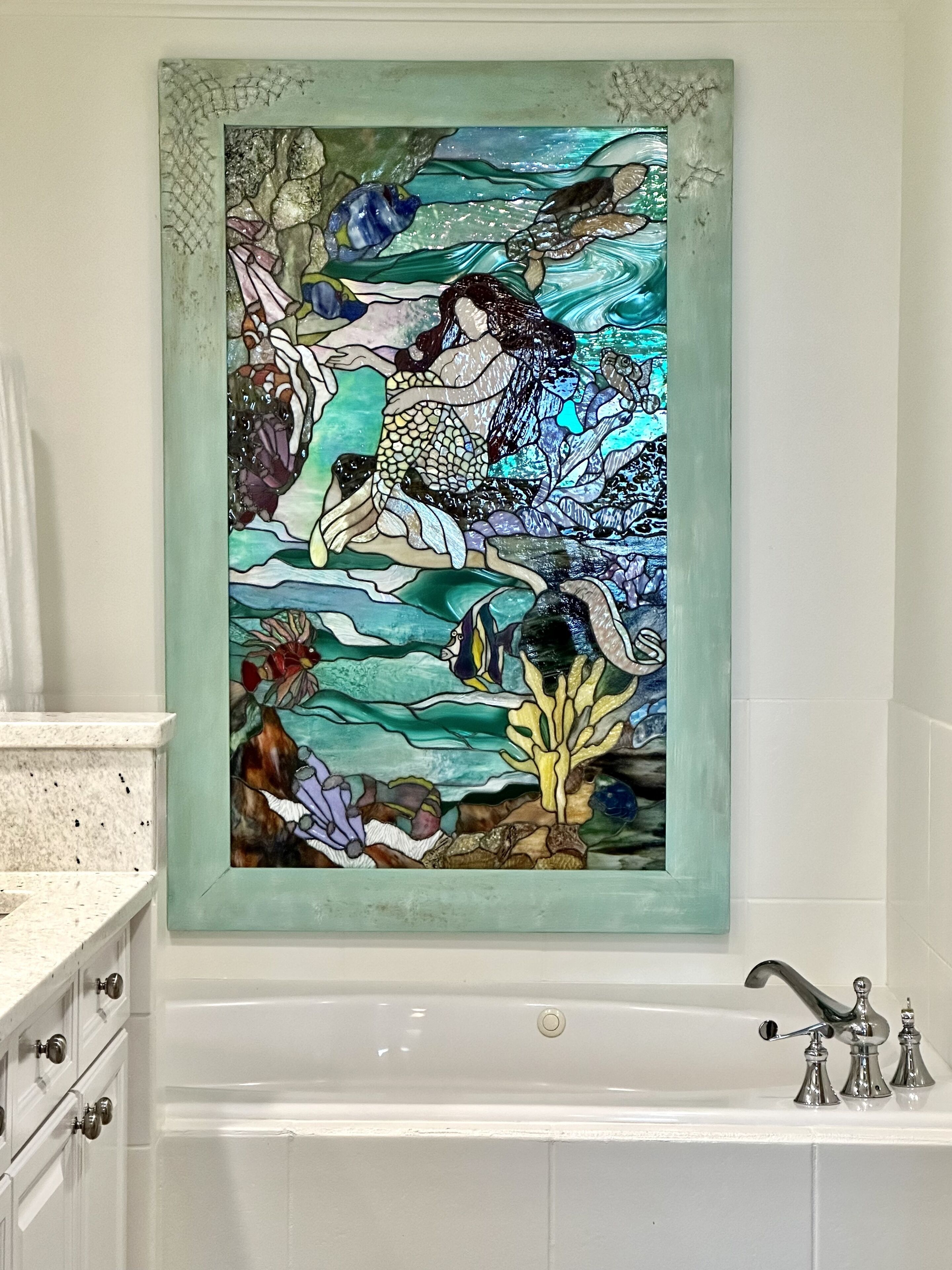 A bathroom with a large stained glass window depicting a mermaid scene.