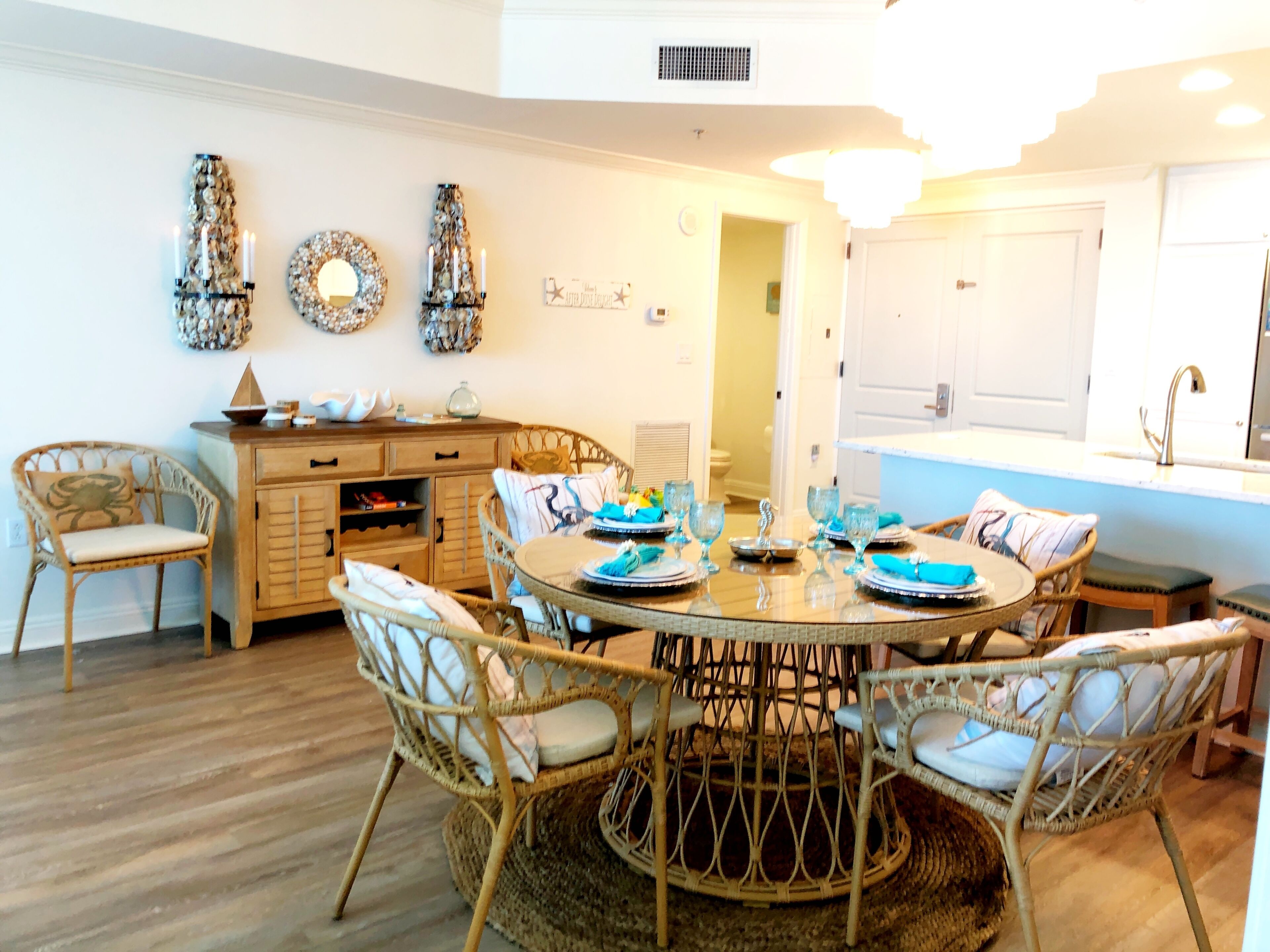 Zona pranzo con tavolo rotondo circondato da sedie in vimini, un mobile contenitore in legno con cassetti e decorazioni murali.