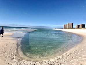 A beach with clear water, footprints, and high-rise buildings in the background.