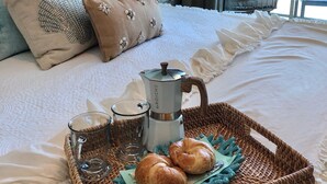 Ein ordentlich bezogenes Bett mit einem Tablett mit Croissants, einer Kaffeemaschine und Gläsern.