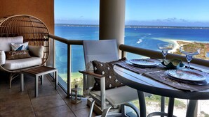 Ein Balkon mit Blick auf das Meer, ein Korbstuhl, ein Tisch mit Tellern und Gläsern sowie eine kleine Laterne.