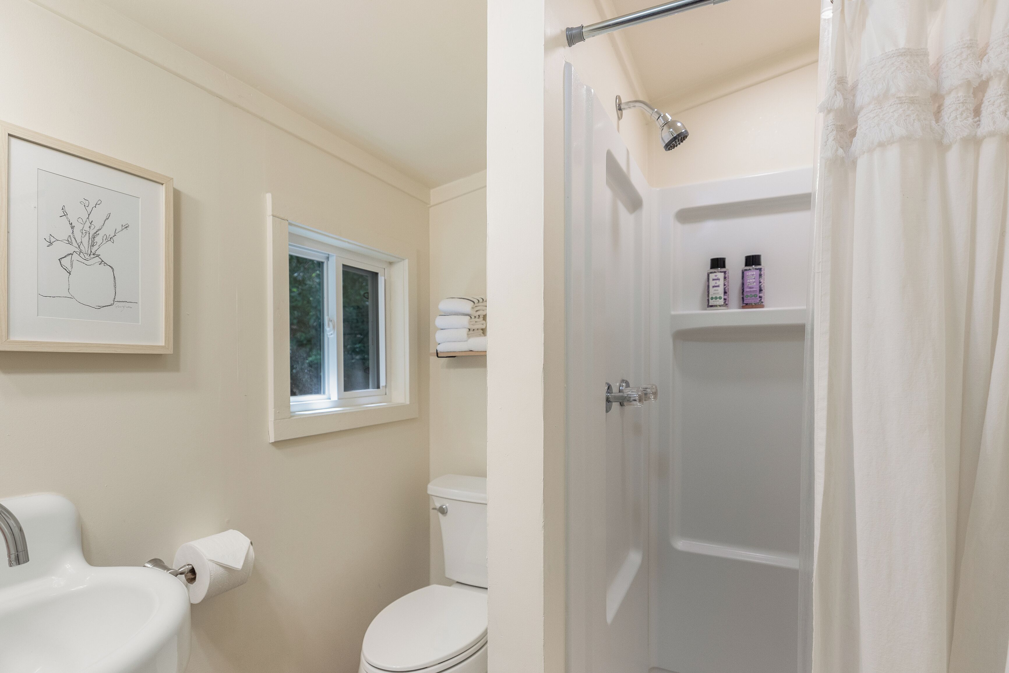 A bathroom with a toilet, sink, and shower. There is a window above the toilet and a shower curtain.