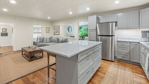 A modern kitchen with grey cabinets, a stainless steel refrigerator, and a large island.