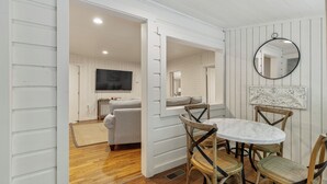 A dining area with a round table and four chairs, a television in the background, and a mirror on the wall.
