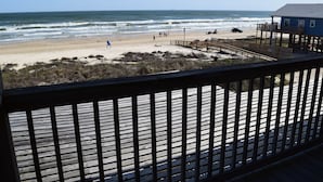 A beach view from a wooden deck with a pier extending into the ocean. - Amazing 5-bedroom beachfront home waiting for your getaway, sleeps 16 (Surfside Beach)