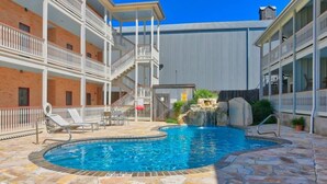 En swimmingpool med stenterasse, et lille vandfald og et overdækket område med balkon.