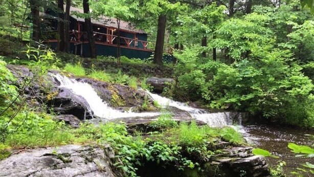 A natural waterfall in a forested area with a wooden structure in the background. - Remote Waterfall Cabin at Swiftwater Acres (Millrift)