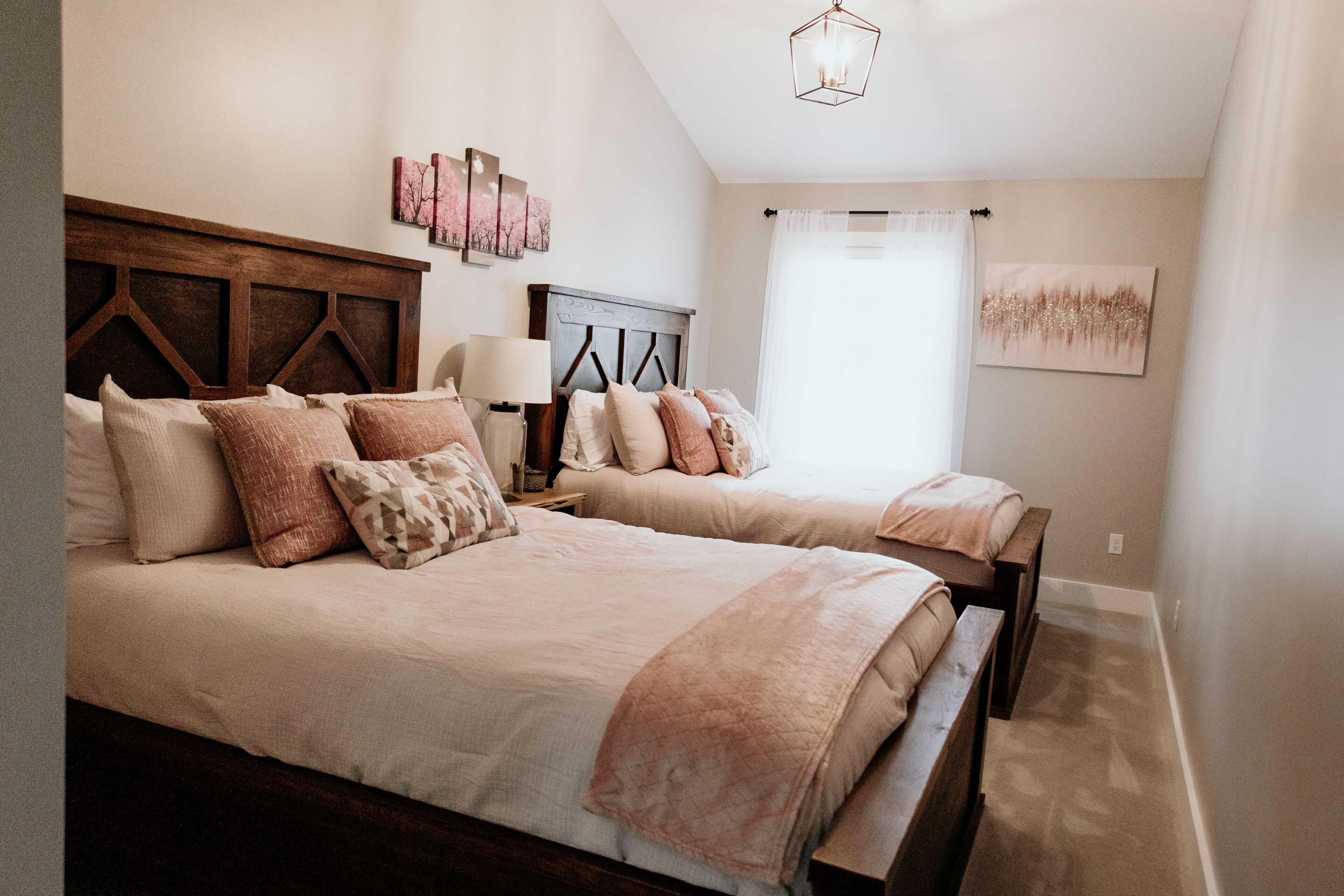 Een slaapkamer met twee bedden, een houten hoofdbord, een nachtkastje met een lamp en kunst aan de muren.