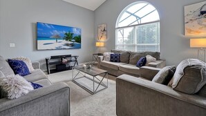 Un salon spacieux doté d’une grande fenêtre, d’un ventilateur de plafond, d’un téléviseur à écran plat et d’une table basse.