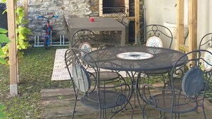 A covered outdoor area with a stone wall, a brick oven, and a table with chairs. - Ciclamino Apartment Residenze Lariane (Colico Piano)