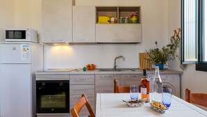 Eine moderne Küche mit Einbauofen, Mikrowelle und Kühlschrank. Es gibt einen Esstisch mit Stühlen, eine Spüle und ein Fenster mit Vorhängen.