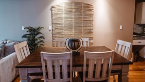 A dining area with a wooden table, four chairs, a decorative vase, and a textured wall panel. - The Watermark Suite (Drumheller)