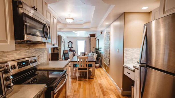 A modern kitchen with stainless steel appliances, a wooden dining table, and a view into the dining area. - The Watermark Suite (Drumheller)
