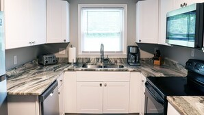 Een moderne keuken met witte kasten, een marmeren aanrechtblad, een inbouwoven en een raam met jaloezieën.