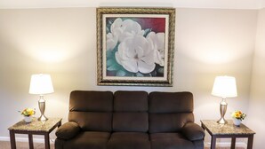 Een bruine bank tegen een muur met een lijstwerk schilderij van bloemen. Twee kleine tafels met lampen en bloevazen staan aan weerszijden van de bank.