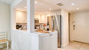 A modern kitchen with white cabinetry, a stainless steel refrigerator, and a built-in island with a sink and countertop.
