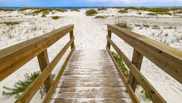 A wooden boardwalk leading to a beach with sand dunes and the ocean in the background.