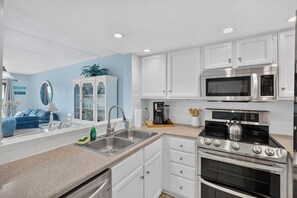 Una cocina moderna con muebles blancos, electrodomésticos de acero inoxidable y una pared de acento azul.