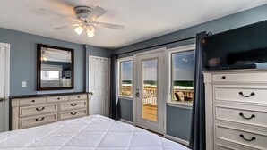 Een slaapkamer met een bed, een dressoir, een plafondventilator en een balkon met uitzicht.
