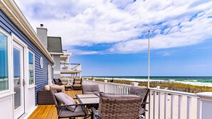 Een houten terras met buitenmeubilair, een witte balustrade en uitzicht op de oceaan.