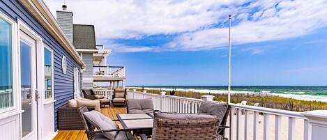 A wooden deck with outdoor furniture, a white railing, and a view of the ocean.
