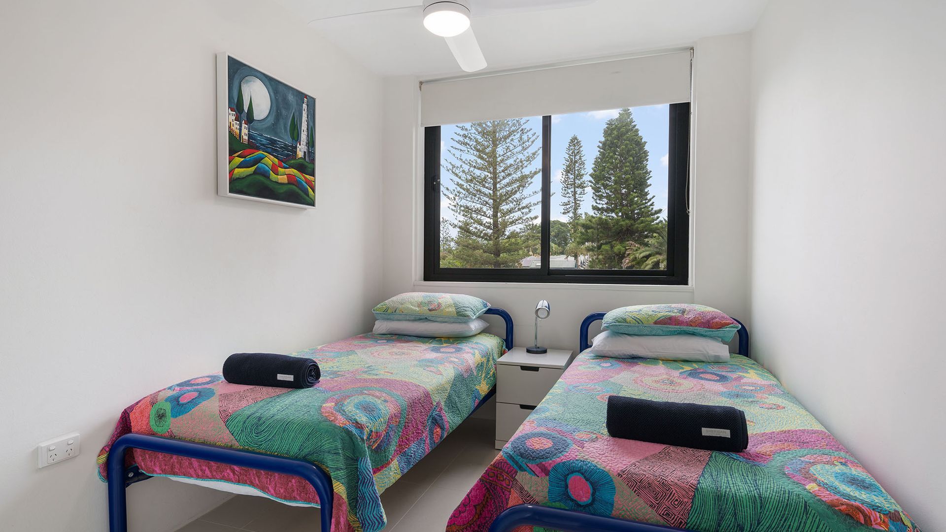 Una camera da letto con due letti singoli, una finestra vista alberi e un quadro appeso al muro.