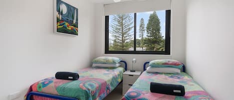 Una camera da letto con due letti singoli, una finestra vista alberi e un quadro appeso al muro.