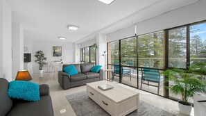 A modern living room with a sofa, coffee table, and large windows offering a view of the outdoors.