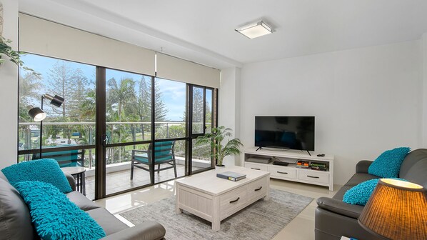 A modern living room with a large TV, comfortable seating, and a balcony with a view.