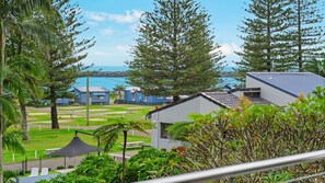 A coastal property with a view of the sea, featuring several blue cabins, a grassy lawn, and a variety of trees.