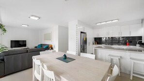 A modern kitchen with white cabinetry, a built-in refrigerator, and a dining area with a light-colored table and white chairs.
