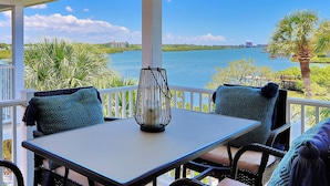 A covered outdoor seating area with a table and chairs, overlooking a body of water and greenery.