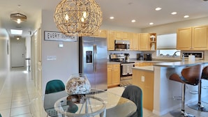 A modern kitchen with a stainless steel refrigerator, a microwave, and wooden cabinets. There is a glass table with chairs and a decorative vase.