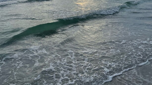 A beach with waves and a sunset.