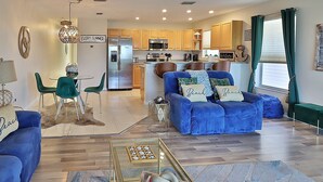 A modern living room with a blue sofa, a glass coffee table, and a dining area with a table and chairs.