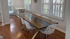 Un espace repas avec une longue table en bois, des chaises blanches et un ventilateur de plafond.