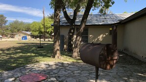 A backyard with a metal barrel, a red circular object, and a bucket on a stone-paved area. - Casa Amigos (Concan)