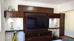 A modern living room with a large flat-screen TV, wooden cabinets, and two small side tables with potted plants. - Jacuzzi Pool Spa Ocean View 4bd 5ba House (El Sauzal)